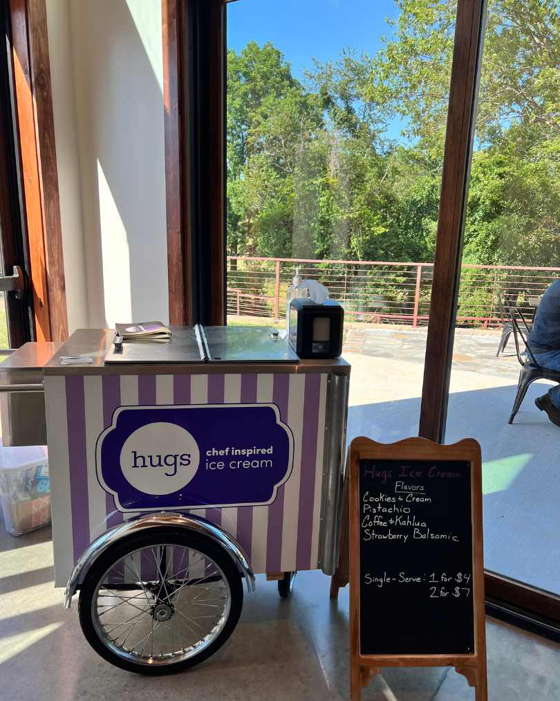 Hugs Ice Cream cart displaying flavors like Pistachio and Cookies & Cream, in a bright setting with outdoor view, showcasing ice cream catering for events in Northwest Arkansas.