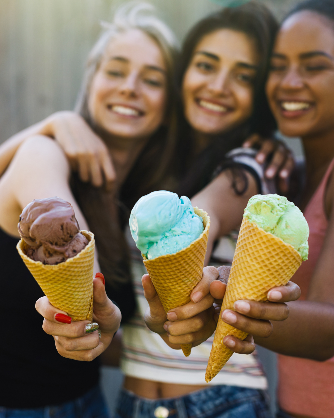 Three friends joyfully holding colorful ice cream cones, featuring chocolate, blue, and green flavors, celebrating the shared experience of enjoying Hugs Ice Cream.